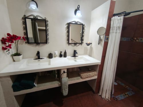 Moderno lavabo de baño en villa Casa Punta Perula con doble lavamanos, espejos decorativos, flores rojas y área de ducha