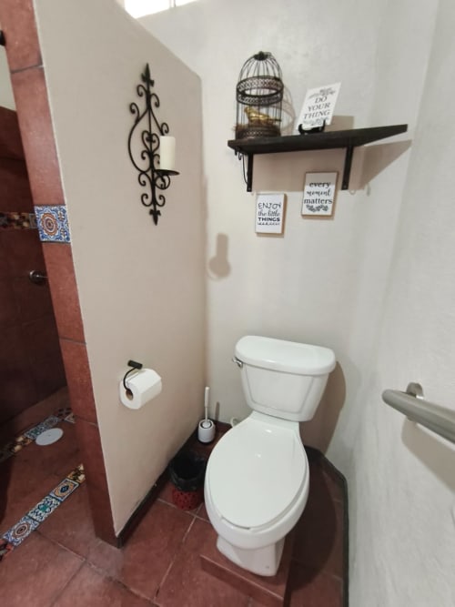 Baño de la villa Casa Punta Perula con inodoro blanco, piso de azulejos oscuros, estantes decorativos y carteles inspiracionales en la pared