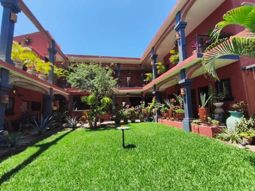 Colorido patio con jardín exuberante, plantas de palma y arquitectura roja en Casa Punta Perula Boutique Hotel, Punta Perula