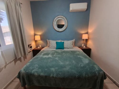 Dormitorio moderno en Casa Punta Perula con pared de acento en turquesa, espejo circular, cama queen con cojines decorativos y ambiente cálido