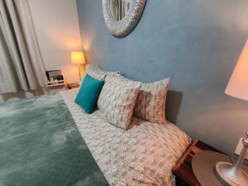 Acogedora habitación en Casa Punta Perula con almohada turquesa, ropa de cama texturizada, lámpara de noche, paredes azules y detalles decorativos