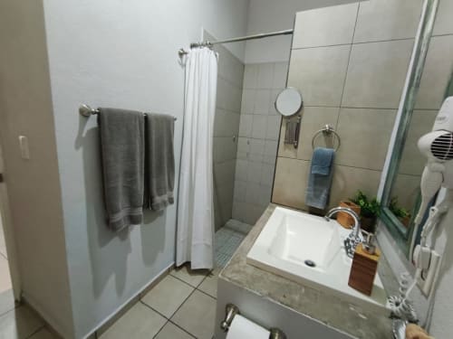 Baño moderno con paredes de azulejos blancos, lavabo, espejo, ducha con cortina blanca y toallero en Casa Punta Perula