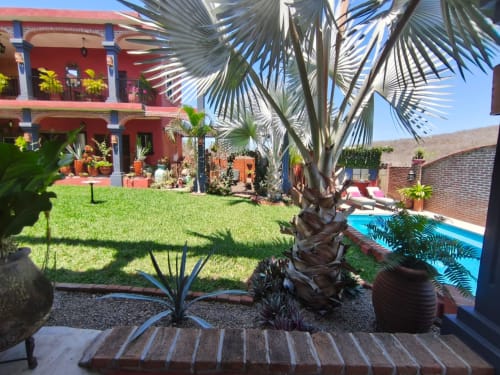 Patio de Casa Punta Perula con edificio colonial rojo, palmeras, piscina y vistas a las montañas en Punta Perula, México