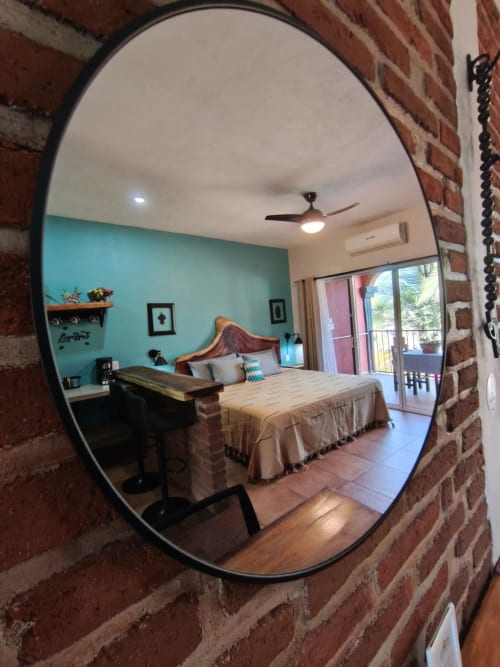 Espejo circular reflejando dormitorio turquesa con cama, escritorio y balcón en Casa Punta Perula Boutique Hotel, Punta Perula