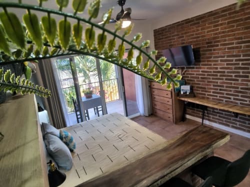 Dormitorio con cama dosel de madera, planta en maceta, pared de ladrillo, TV, escritorio y puertas de cristal que se abren al jardín de la villa Punta Perula