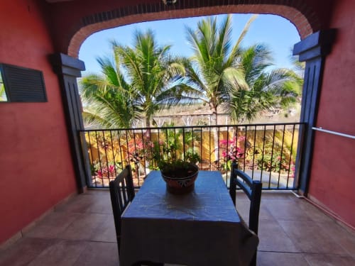 Balcón de villa roja con mesa azul con vistas a jardines tropicales y palmeras en Casa Punta Perula, Punta Perula México
