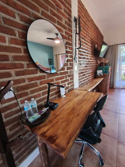 Espacio de trabajo moderno con superficie de madera contra pared de ladrillo rojo, espejo redondo y silla negra en villa Casa Punta Perula