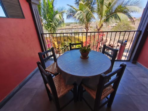 Mesa de comedor azul con sillas negras en la terraza con vistas a palmeras y piscina en Casa Punta Perula, Punta Perula México