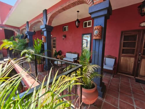 Colorido patio colonial de Casa Punta Perula con muros rojo brillante, pilares azules, palmeras en macetas y decoración tropical