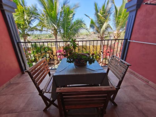 Vista del balcón en Casa Punta Perula con mesa de comedor, sillas de madera, plantas en macetas y palmeras con vistas a Punta Perula