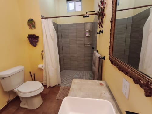 Baño amarillo brillante con inodoro blanco, bañera manchada, espejo de vanidad y ducha tipo walk-in con azulejos grises y cortina blanca en Casa
