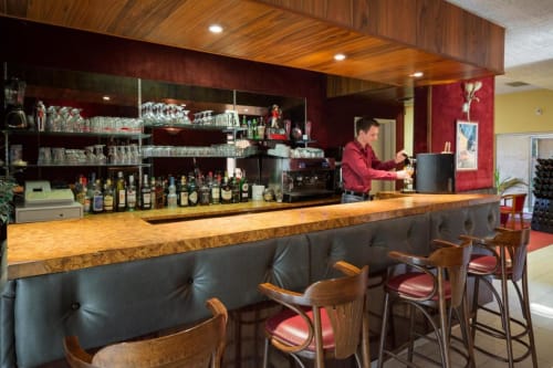 Bar de l'Hôtel de Champagne à Saint-Dizier avec comptoir en bois, tabourets en cuir et barman préparant des cocktails