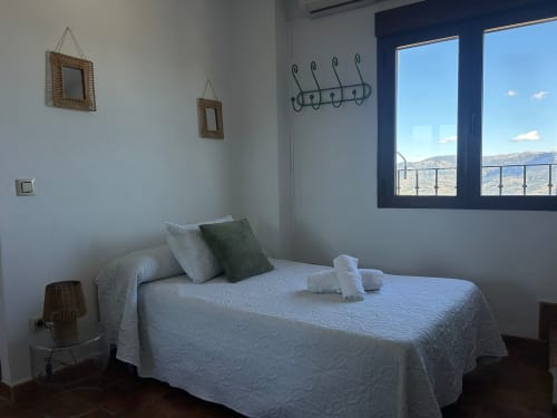 Dormitorio luminoso en la casa rural Casa de la Aguadora en Iznatoraf con ropa de cama blanca, vistas a las montañas a través de grandes ventanales y