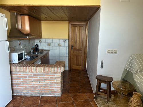 Acogedora cocina de pueblo en Iznatoraf con encimera de ladrillo, azulejos decorativos, armarios de madera y suelo de terracota en Casa de la