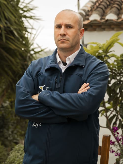 Miembro del personal masculino con chaqueta azul marino de brazos cruzados en jardín exuberante del hotel Escanda Building Solutions