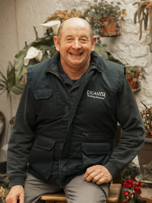 Smiling man in Escanda Building Solutions jacket seated in hotel garden with potted plants