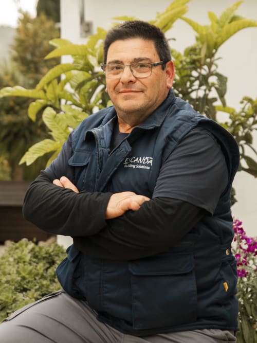 Man in Escanda Building Solutions vest poses in greenhouse with plants and flowers