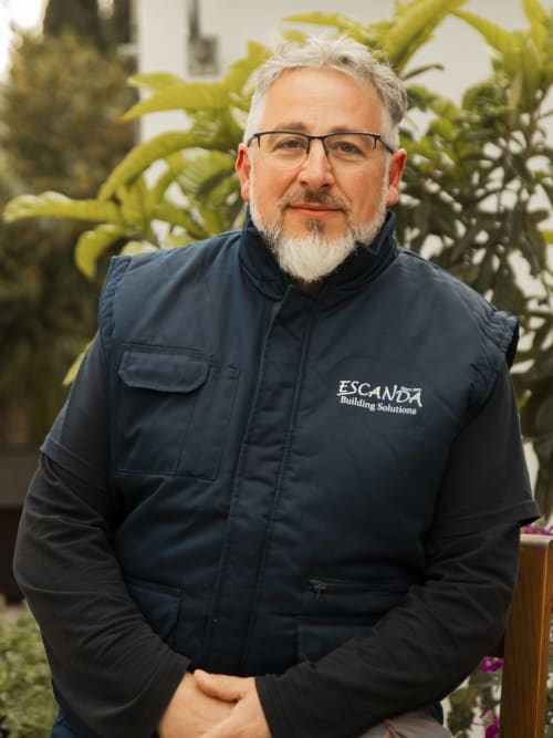 Middle-aged man with gray beard wearing Escanda Building Solutions jacket, posed outdoors with cacti background