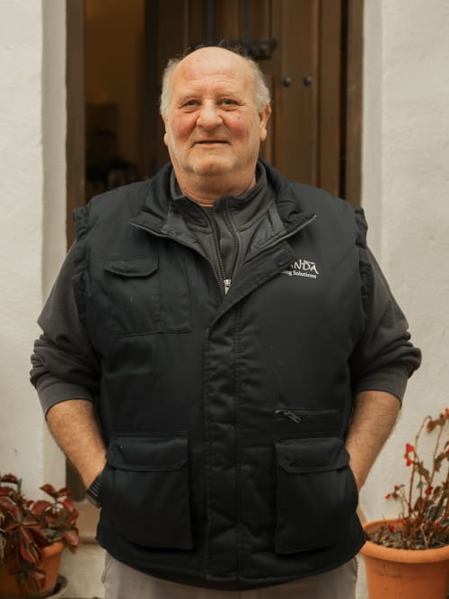 Man in black Escanda Building Solutions vest standing in hotel corridor with potted plants