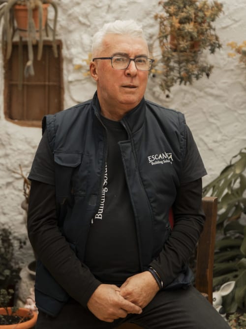 Senior man in Escanda Building Solutions vest seated in courtyard with white stone walls
