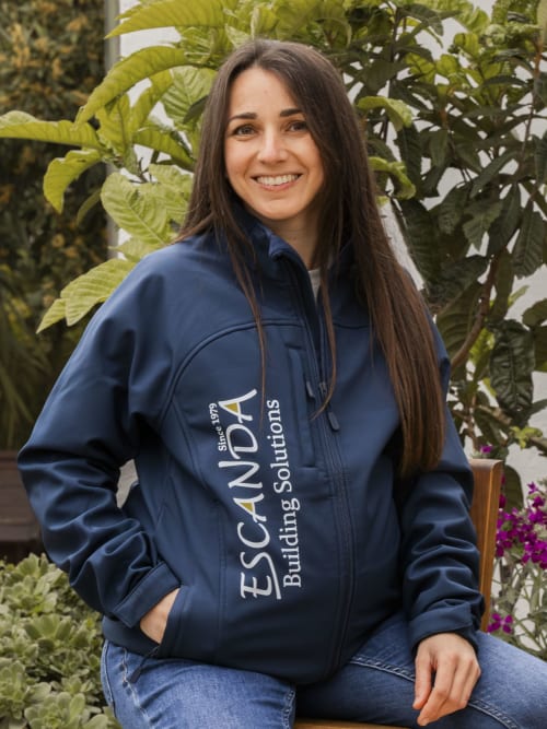Woman in EscandA Building Solutions navy jacket in front of lush green plants, smiling at camera