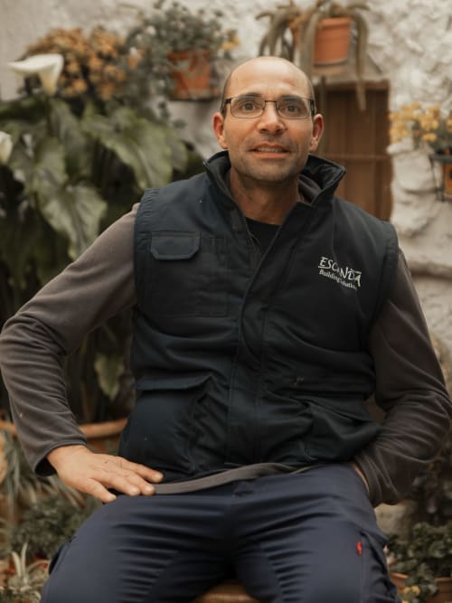 Man in glasses wearing Escanda Building Solutions vest seated outdoors with potted plants