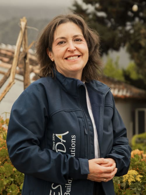 Woman smiling in navy jacket at Escanda Building Solutions hotel in Spain, with garden and architecture backdrop