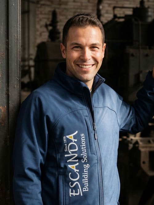 Smiling man in blue Escanda Building Solutions jacket standing in industrial setting