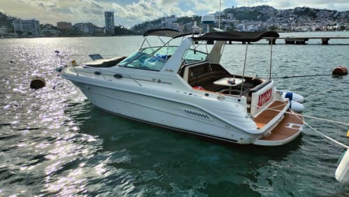 Lancha rápida blanca amarrada en las aguas turquesas de Acapulco con paisaje urbano y resorts en la ladera
