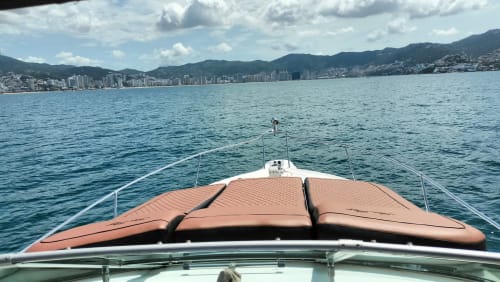 Vista de la cubierta de un lujoso yate con vistas a las aguas turquesas y la costa de Acapulco, con montañas de fondo