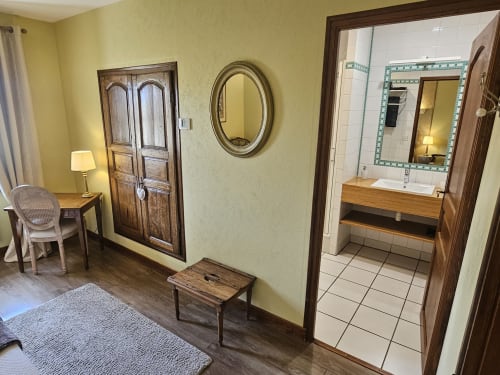 Entrée de chambre du Château de Ribourdin aux murs jaunes, portes en bois, miroir ovale, coin bureau et accès salle de bain