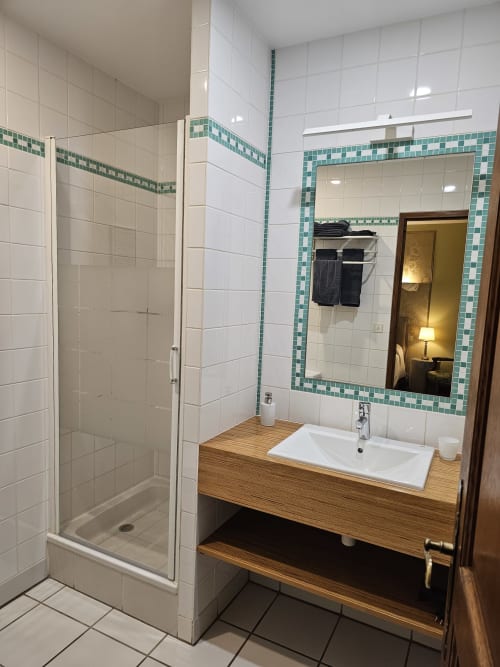 Salle de bains moderne au Château de Ribourdin avec douche à l'italienne, meuble vasque en bois, carrelage bleu-vert et grand miroir
