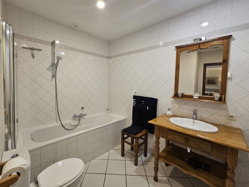 Château de Ribourdin bathroom with white tile, wooden vanity, mirror, bathtub with shower, and toilet in Chevannes