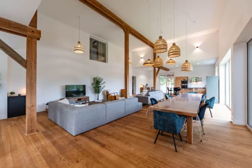 Espace de vie ouvert et moderne avec poutres en bois, canapé gris, table à manger et luminaires suspendus au Refuge des Brumes, France