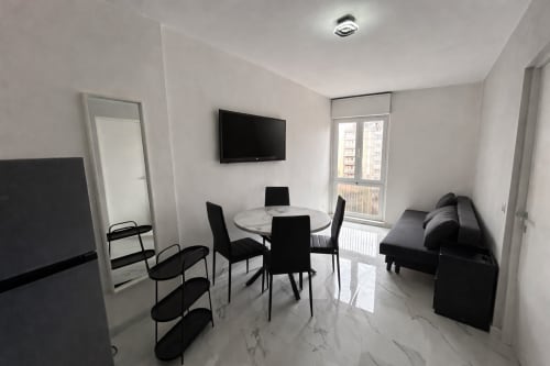 Moderno loft all'hotel Anthea a Lignano Sabbiadoro con tavolo da pranzo, sedie nere, divano, TV e vista sulla città