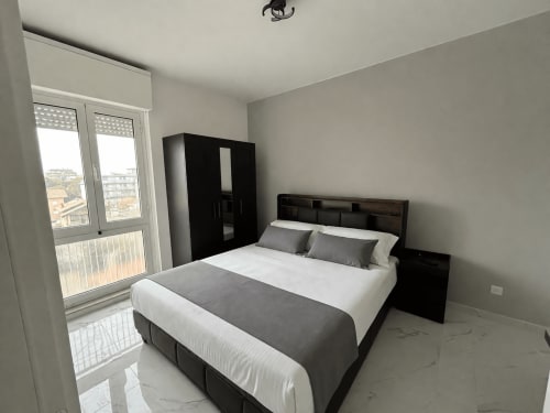Camera moderna con letto nero, biancheria bianca, dettagli grigi e vista sulla città dal balcone dell'Hotel Anthea Lignano