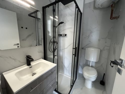 Bagno moderno con piastrelle in marmo, box doccia con cornice in vetro nero, lavabo bianco e toilet all'hotel Anthea