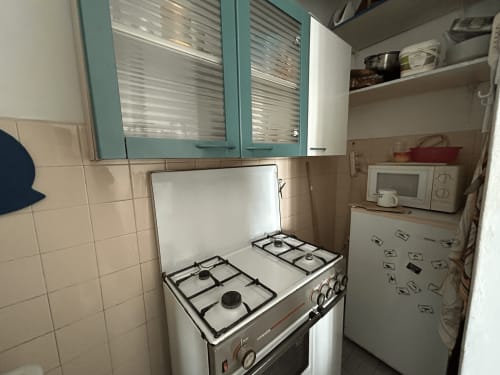 Angolo cucina compatto nell'appartamento Anthea a Lignano Sabbiadoro, con fornello a gas, piano cottura bianco e pensili turchesi