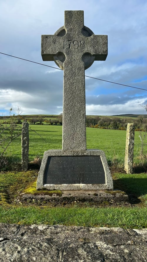 Celtic cross memorial dated 1998 in rural Wicklow countryside with green fields and cloudy sky