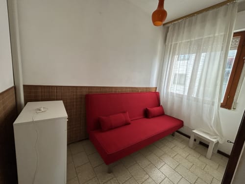 Comfort apartment living room at Anthea hotel in Lignano Sabbiadoro with red sofa, white appliance, and balcony access