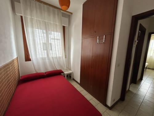 Comfort apartment bedroom at Anthea hotel in Lignano Sabbiadoro with red bed, wooden wardrobe, and sheer curtains