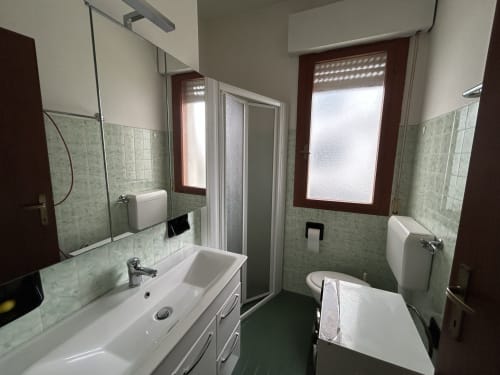 Modern bathroom in Comfort Apartment at Anthea Hotel, Lignano Sabbiadoro with white sink, toilet, shower, and green tile