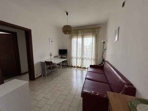 Comfortable apartment living room with burgundy sofa, dining table, TV, and balcony access at Anthea hotel, Lignano
