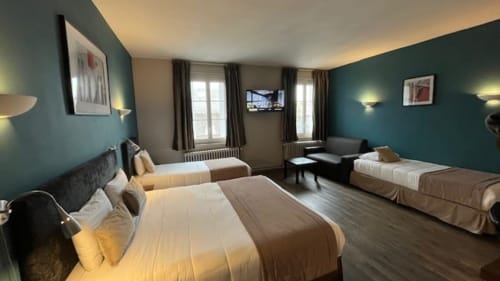 Spacious family room at Hôtel Des Cèdres in Orleans with teal walls, multiple beds, TV, and city views