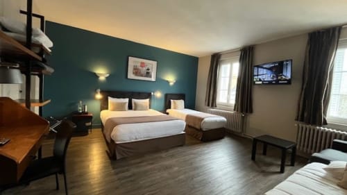 Hôtel Des Cèdres family room with two beds, teal accent wall, desk, TV and city view windows in Orleans
