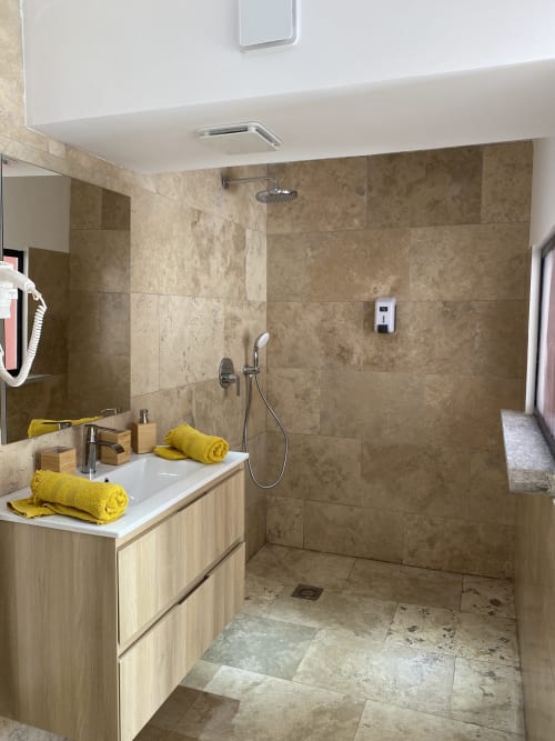 Baño moderno en Casa Di Floumy B&B en Calvi con azulejos de travertino, ducha abierta y toallas amarillas