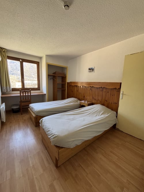 Chambre quadruple lumineuse au Centre Sportif d'Altitude Briançon avec deux lits en bois, fenêtre, bureau et parquet