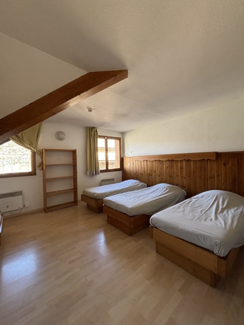 Chambre quintuple au Centre Sportif d'Altitude de Briançon avec trois lits, poutres bois, fenêtres et lambris