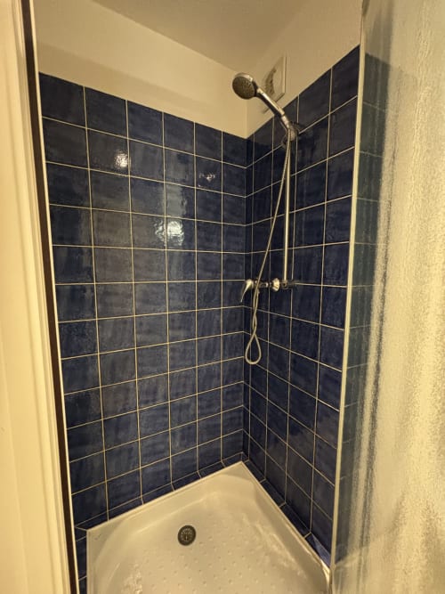 Cabine de douche avec carrelage bleu foncé et pommeau de douche au plafond à l'hôtel Centre Sportif d'Altitude de Briançon