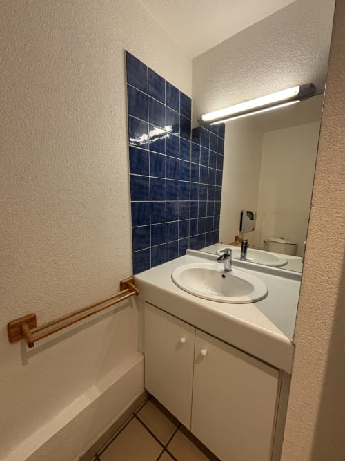 Salle de bain moderne avec lavabo blanc, dosseret en carrelage bleu foncé et miroir à l'hôtel sports de Briançon